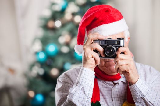 Senior man in Santa's hat taking photo on Christmas background