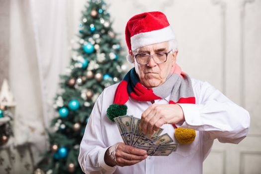 Senior man in Santa's hat holding money over Christmas background