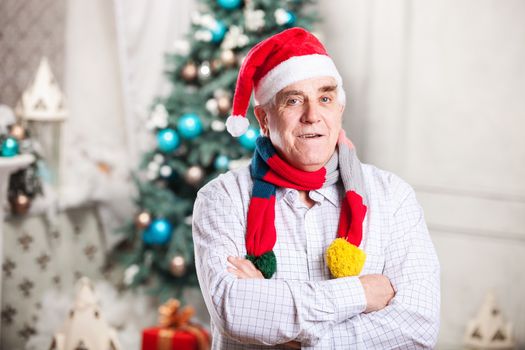 Portrait of mature man in Santa's hat and bright scarf standing with arms crossed over Christmas background