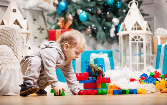 Cute toddler boy playing with building blocks at Christmas tree