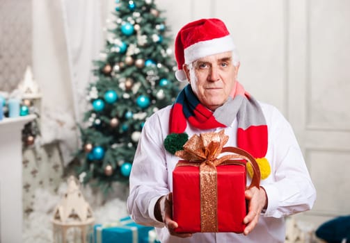 Senior man holding a red gift box on Christmas background