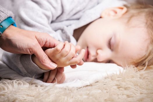 Closeup view of mother holding son's hand while he is sleeping