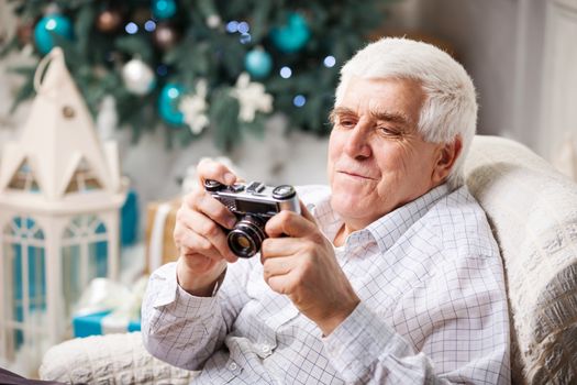 Senior man looking at display of retro style camera and smiling against Christmas background