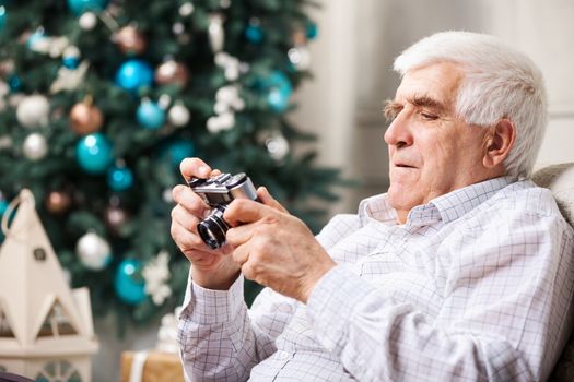 Senior man looking at display of retro style camera and smiling against Christmas background