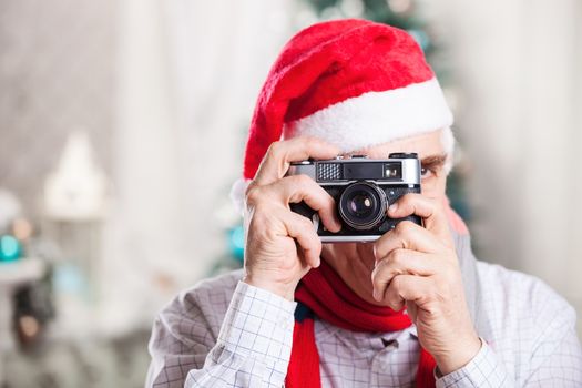 Senior man in Santa's hat taking photo on Christmas background