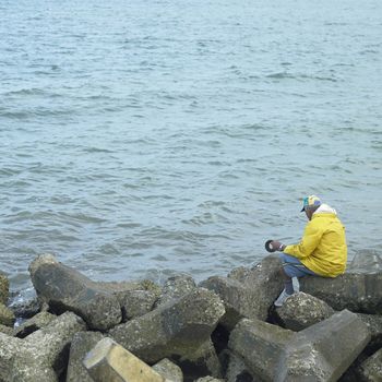 Old man in a yellow rain coat fishing