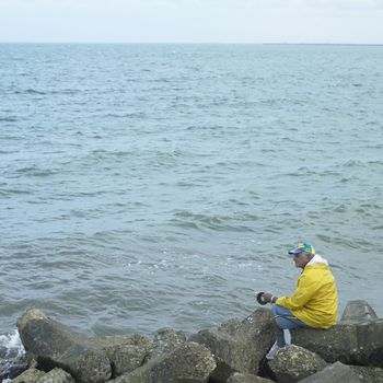 Old man in a yellow rain coat fishing