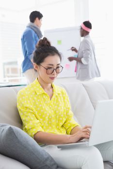 Young creative woman using laptop on couch in creative office