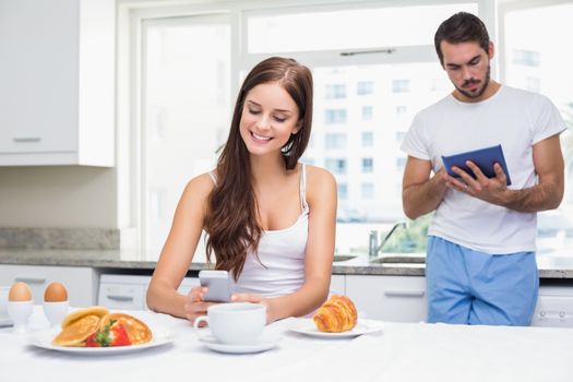 Young couple using technology at breakfast at home in the kitchen