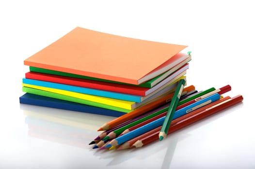 Horizontal shot of pile of multicolored workbooks and twelve colored pencils