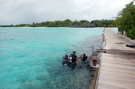 Divers in the sea near timber pier, Maldives