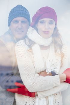 Happy couple in warm clothing seen through glass window