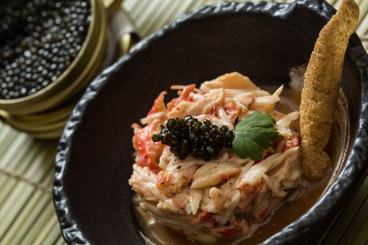 Crab meat in a dish on wood table with black caviar