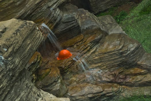 orange construction helmet under a waterfall on the rocks