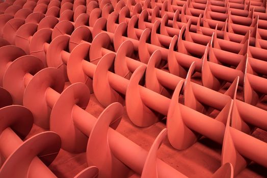 Red painted metal screws for industrial screw conveyors at a paintshop.