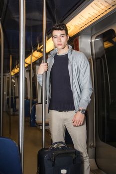 Young man standing in subway train going on vacation with trolley suitcase