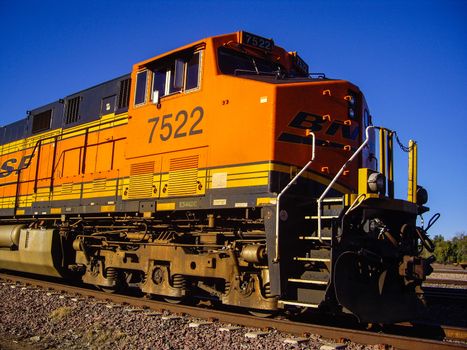 Distinctive orange and yellow Burlington Northern Santa Fe Locomotive freight train No. 7522 on the tracks at the town of Needles, California. Photo taken in February 2013.