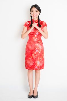 Happy Chinese New Year!! Portrait of Asian Chinese girl blessing, in traditional red qipao standing on plain background.