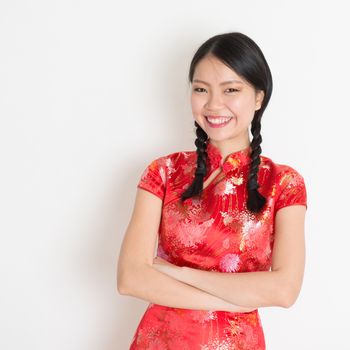 Portrait of Asian Chinese girl smiling, in traditional red qipao standing on plain background.