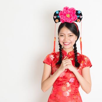 Portrait of Asian Chinese girl with princess hat greeting, in traditional red qipao standing on plain background.