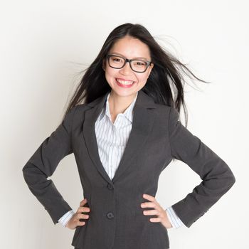 Confident young Asian business woman smiling at camera, standing on plain background.