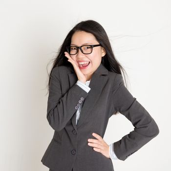 Surprised Asian business woman looking at camera and smiling, standing on plain background.