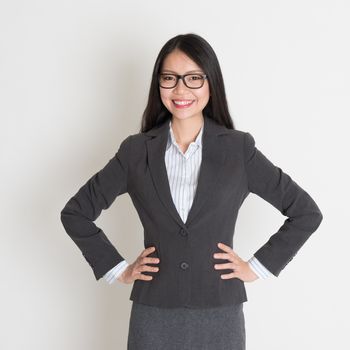 Young Asian business woman smiling at camera, standing on plain background.