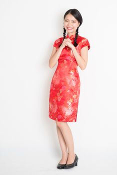 Happy Chinese New Year!! Portrait of Asian Chinese girl blessing, in traditional red cheongsam standing on plain background.