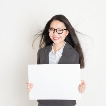 Asian business woman holding a blank card board with copy space, standing on plain background.