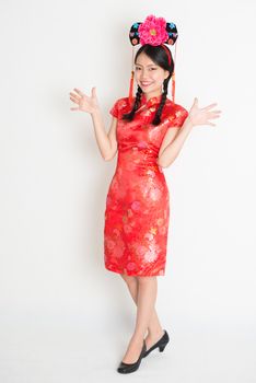 Portrait of full length Asian Chinese girl with princess hat, in traditional red qipao standing on plain background.