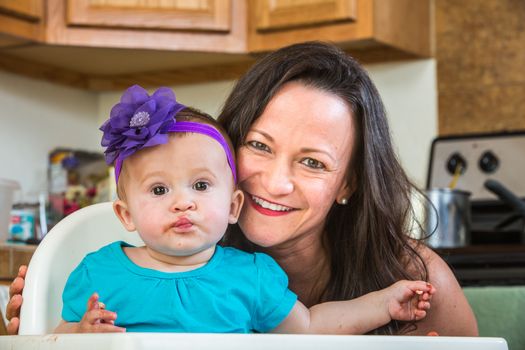 Mother in messy kitchen smiles as baby eats