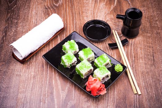 sushi roll set in green caviar with ginger, soy sauce, towel and chopsticks on wooden background 