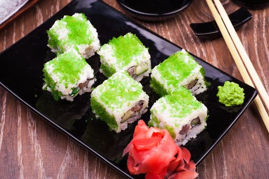 sushi roll set in green caviar with ginger and chopsticks on wooden background 