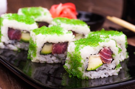 sushi roll set in green caviar with ginger, soy sauce, towel and chopsticks on wooden background 