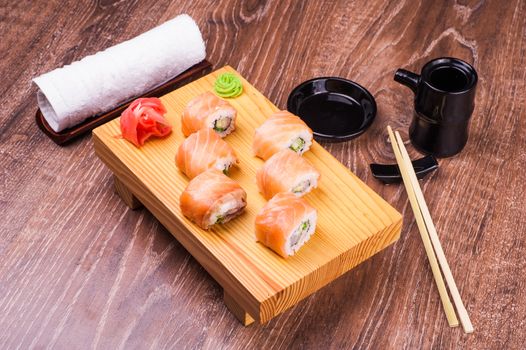 sushi roll set covered in salmon on wooden background 