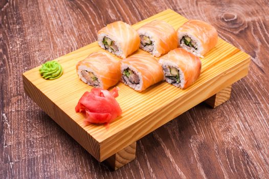 sushi roll set covered in salmon on wooden background 