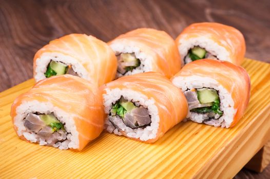 sushi roll set covered in salmon on wooden background 