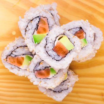 inside out sushi roll with salmon and avocado on wooden background 