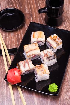 eel sushi roll  with ginger, soy sauce, towel and chopsticks n wooden background