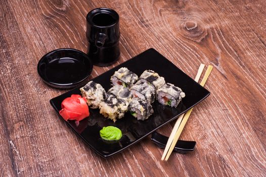 tempura sushi roll with ginger, soy sauce and chopsticks on wooden background