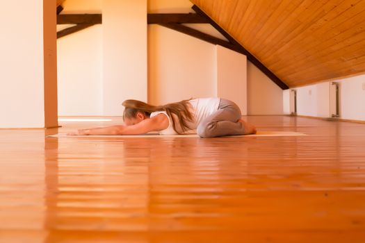 A young Woman practicing Yoga in a large attic Studio.