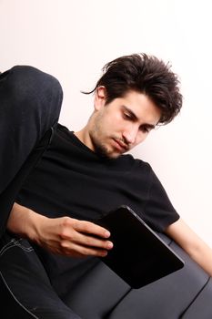 A young hispanic man sitting on the sofa holding a Tablet PC.