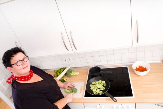 Mature overweight woman cutting vegetables in the kitchen.
