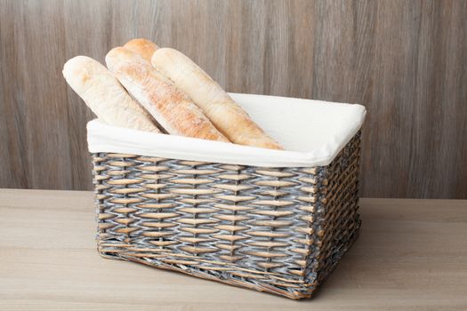 Stack of traditional fresh-baked French bread loafs baguette served in woven basket on wooden background