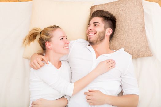 A happy young couple hugging in bed.
