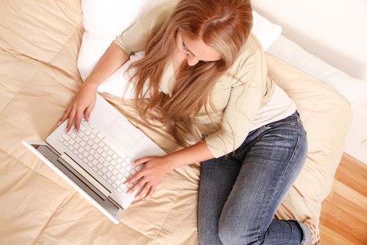 Beautiful blonde woman working on laptop at home in bed.
