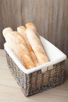 Stack of traditional fresh-baked French bread loafs baguette served in woven basket on wooden background