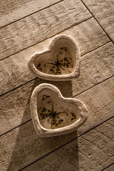Two heart decorations on a white whashed wooden table in low directional light of the late afternoon.