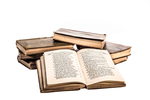 Old neglected books placed in to a small heap of two stacks with one of the books open and leaning against the stacks facing the viewer, all on a white background.