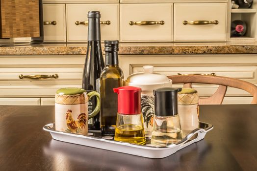 assorted condiments on a tray at a table inside a private house whith french style classical kitchen cupboards in the background.